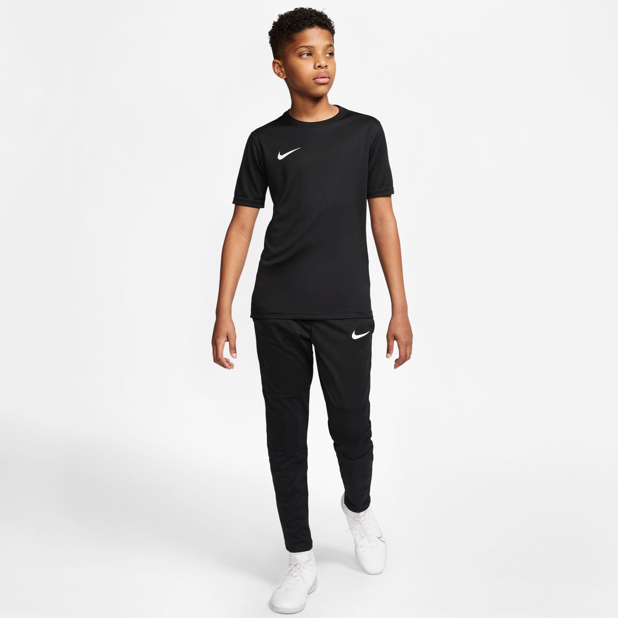 Boy wearing Nike Dri-fit Park VII Shirt Short Sleeve in Black and black Nike Jogging Bottoms and White Nike Trainers