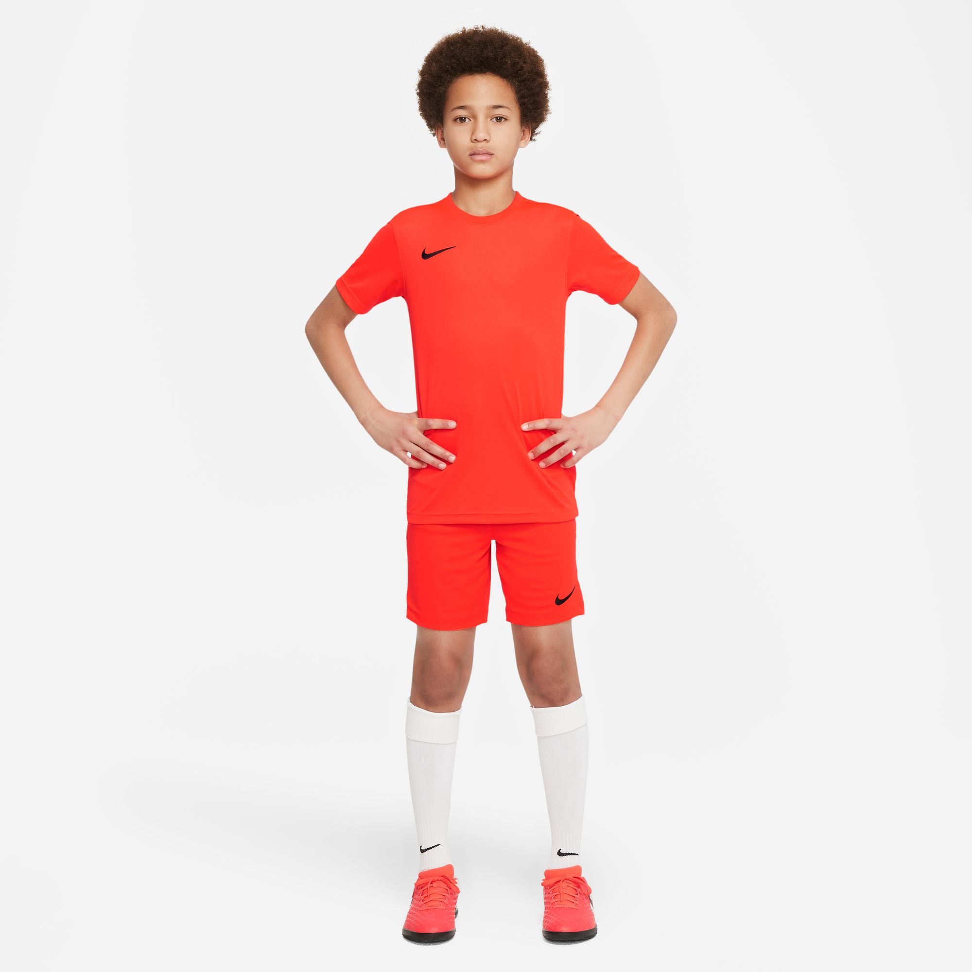 Boy wearing Nike Dri-fit Park VII Shirt Short Sleeve Shirt in Bright Crimson Black with matching shorts and boots